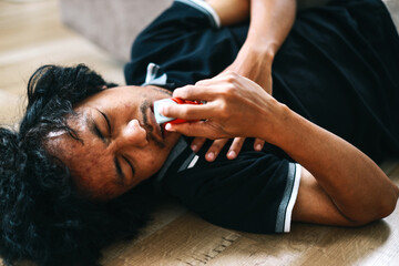Young man with breathing difficulties using an inhaler during asthmatic attack on the floor - obrazy, fototapety, plakaty