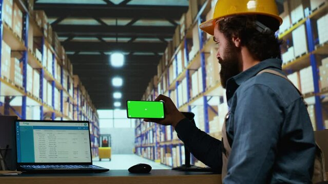Warehouse manager looks at greenscreen on smartphone display, working on parcel shipment and delivery in industrial depot. Quality control advisor using blank copyspace mockup screen.