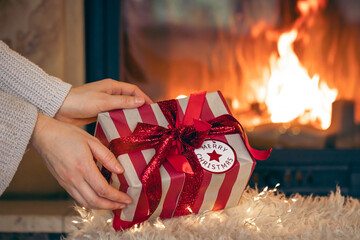 Christmas gift box by the fireplace in female hands.