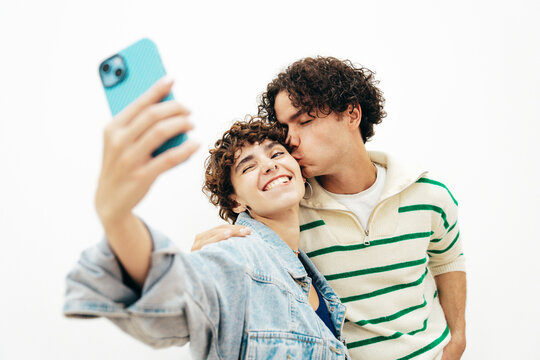 Smiling beautiful woman and her handsome boyfriend with curls hairstyle. Happy cheerful family having tender moments in white interior in studio.Pure cheerful models hugging. take selfie photos