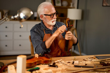 Senior carpenter craftsman carving wood and making violin instrument
