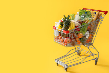 Shopping cart full of groceries on yellow background. Space for text