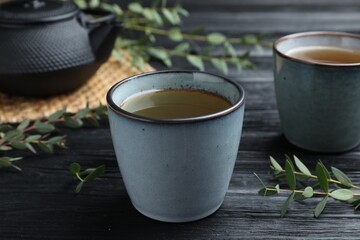 Cup of aromatic eucalyptus tea on black wooden table, closeup