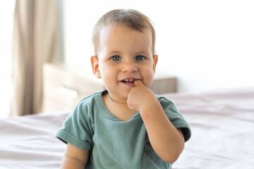 close-up portrait of a cute 10 month old baby with his finger in his mouth, drooling, new teeth growing, baby looking at the camera.