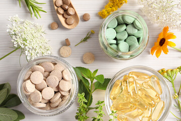 Different pills, flowers and herbs on white wooden table, flat lay. Dietary supplements