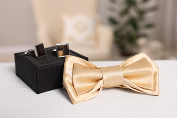 Stylish beige bow tie and box with cufflinks on white wooden table, closeup