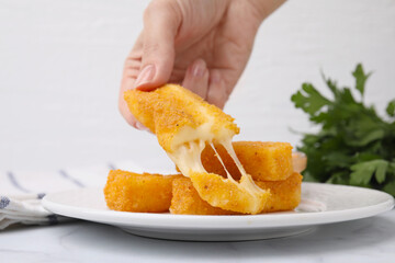 Woman taking tasty fried mozzarella stick from plate at table, closeup