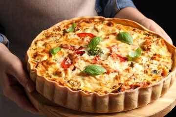 Woman holding board with tasty quiche on black background, closeup