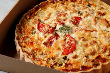 Tasty quiche with tomatoes and cheese in open box on table, closeup