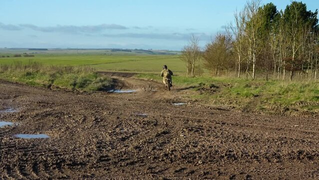 British army Paratrooper riding a Qiulong Surron Sur-Ron Firefly electric motorcycle along a muddy track on a military exercise