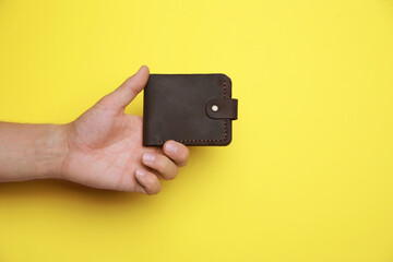 Man holding leather wallet on yellow background, closeup. Space for text