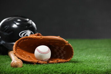 Baseball bat, batting helmet, leather glove and ball on green grass against dark background. Space...