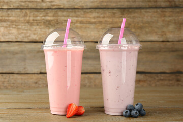 Plastic cups with different tasty smoothies and fresh fruits on wooden table
