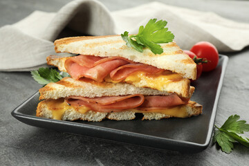 Tasty sandwiches with ham, parsley and melted cheese on grey textured table, closeup
