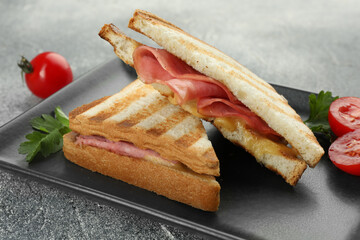 Tasty sandwiches with ham, parsley, tomatoes and melted cheese on grey textured table, closeup