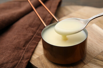 Taking tasty condensed milk with spoon at table, closeup