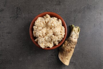 Bowl of tasty prepared horseradish and root on grey table, flat lay