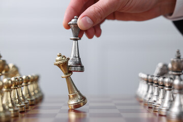 Man with bishop game piece playing chess at checkerboard against grey background, closeup
