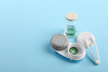 Bottle of solution, case with green contact lenses and tweezers on light blue background. Space for...