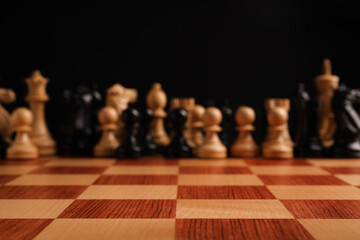 Many chess pieces on wooden checkerboard against black background, selective focus