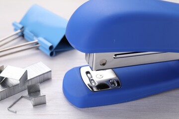 Blue stapler with staples on light wooden table, closeup