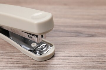 Beige stapler with staples on wooden table, closeup. Space for text
