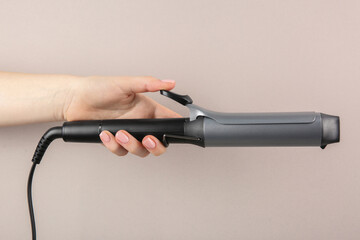 Hair styling appliance. Woman holding curling iron on light grey background, closeup