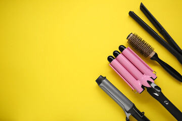 Different curling irons, hair straightener and round brush on yellow background, flat lay. Space...