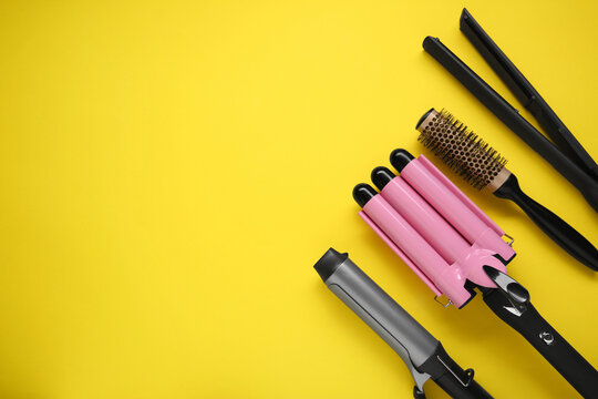 Different curling irons, hair straightener and round brush on yellow background, flat lay. Space for text