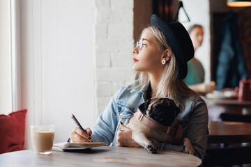 Lifestyle blogger woman working on web tablet with pug dog at pets friendly cafe. Outdoor lifestyle...