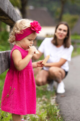 A two-year-old girl in a pink dress tries cookies on a walk
