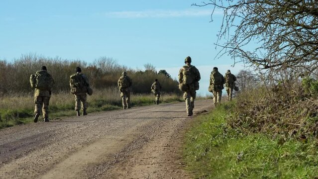 7 male and female British army soldiers tabbing with 25Kg bergens along a dirt road, Wiltshire UK