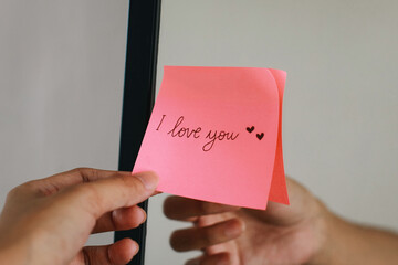 Woman putting a sticky note with phrase I Love You on the mirror.