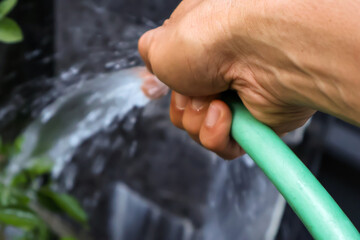 Close up of an asian man's hand watering plants around his house with a green hose