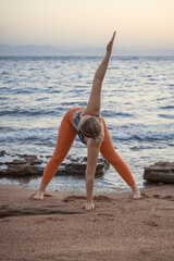 Fototapeta na wymiar Young beautiful lady performing twist yoga pose on the beach at sunrise