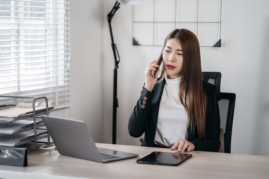 Business woman using smartphone and laptop computer in office. Happy woman, entrepreneur, small business owner working online.