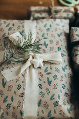 Merry Christmas! Stylish christmas gifts in festive wrapping paper with fir branch, bows, ribbons, vintage ornaments on wooden table. Atmospheric winter holidays preparation