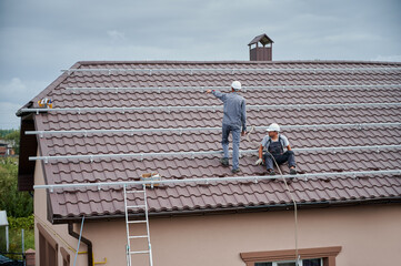 Men mounters prepearing for mounting photovoltaic solar moduls on roof of house. Electricians in...