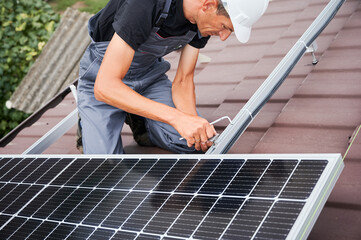 Man technician mounting photovoltaic solar moduls on roof of house. Electrician in helmet installing solar panel system outdoors. Concept of alternative and renewable energy.
