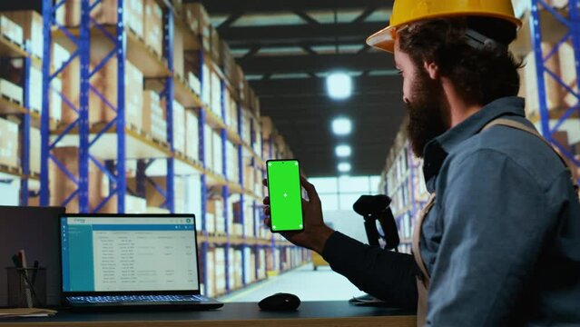 Delivery station associate works with greenscreen display in warehouse depot, checking stock logistics for new parcel shipment. Depot worker shows isolated copyspace template.