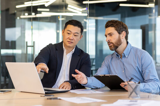Business meeting, two business people serious concentrated discussing strategy and plans, sitting at table with documents inside office at workplace discussing communicating looking at laptop screen.