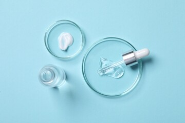 Petri dishes with samples of cosmetic serums, bottle and pipette on light blue background, flat lay