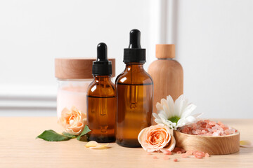 Bottles of cosmetic serum, beauty products, sea salt and flowers on wooden table, closeup