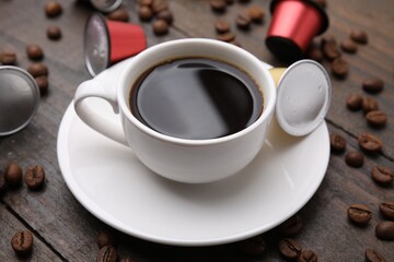 Cup of coffee, capsules and beans on wooden table, closeup