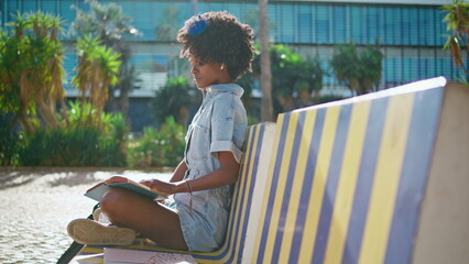 Curly girl learning homework holding book sitting bench outdoor. Student reading