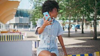 Cute teenager recording video blog on smartphone sitting street. Girl talking