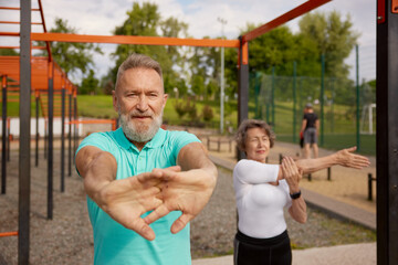 Obraz premium Seniors couple stretching arms before exercise at training field outdoors