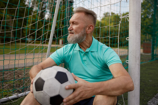 Happy senior man feeling tired after football training on soccer field