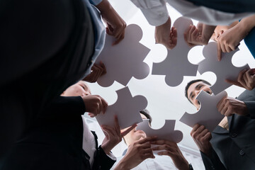 Below view of diverse corporate officer workers collaborate in office connecting puzzle pieces as...