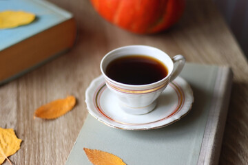 Cup of tea or coffee, plate with desserts, dried oranges, bowl of grapes, scented candles, vintage books, pumpkins and autumn leaves on the table. Autumnal hygge. Selective focus.